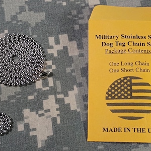 May include: A silver-toned stainless steel ball chain set consisting of one long chain and one short chain. The packaging is a yellow envelope labeled Military Stainless Steel Dog Tag Chain Set with a graphic of the American flag and text Made in the USA.