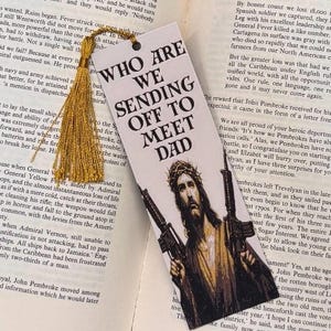 Puede incluir: Marcap&aacute;ginas con el texto "WHO ARE WE SENDING OFF TO MEET DAD" y una imagen de Jes&uacute;s sosteniendo dos rifles. Una borla dorada est&aacute; unida en la parte superior. El fondo es una p&aacute;gina de libro.
