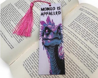 Puede incluir: Un marcapáginas colorido con la frase "MONGO IS APPALLED" y una ilustración de criatura fantástica. Incluye una borla rosa y está colocado en un libro abierto.