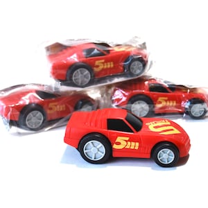 May include: Three red toy race cars with the number 5 printed on them. The cars are in plastic packaging.