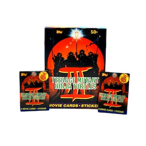 May include: A box of Teenage Mutant Ninja Turtles II trading cards. The box is red, black, and white with a picture of the four turtles on the front. The text on the box reads "Teenage Mutant Ninja Turtles II Movie Cards - Stickers".