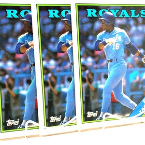 May include: Four baseball cards featuring a baseball player in a blue uniform with the word "ROYALS" printed in green and white. The player is holding a bat and wearing a white helmet. The cards are from Topps.