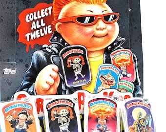 May include: A box of Garbage Pail Kids trading cards featuring a cartoon character with red hair and sunglasses. The box has the text "Collect All Twelve" and "99¢". The cards are individually packaged in plastic wrappers with the text "Garbage Pail Kids" and "Drop Dead!" on them.