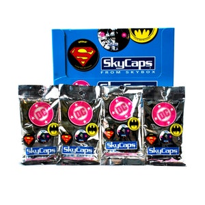 May include: Four silver foil pouches with DC Comics SkyCaps trading cards. Each pouch features a pink DC logo with white stars and a variety of DC Comics characters including Superman, Batman, and Wonder Woman.