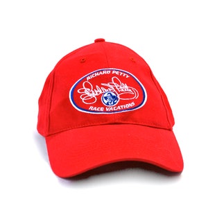 May include: Red baseball cap with a blue and white oval logo featuring Richard Petty's signature and the text "Race Vacations".