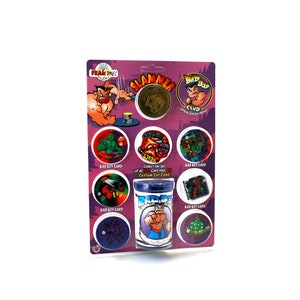 May include: A collection of "Bad Boy" themed game caps and a container, displayed on a purple and white card. The caps feature various cartoon characters and the text "Bad Boy Caps!" The container has a "Bad Boy" logo.