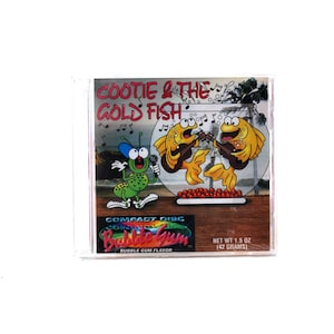 Puede incluir: Una caja de CD con una ilustración colorida de un insecto verde y dos peces amarillos cantando en una pecera. El texto en la caja dice "Cootie & The Gold Fish" y "Bubble Gum Flavor".