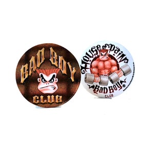 Può includere: Due adesivi rotondi con un logo Bad Boy Club. Un adesivo presenta un personaggio dei cartoni animati con i capelli rossi e uno sfondo marrone. L'altro adesivo presenta un personaggio dei cartoni animati muscoloso che solleva pesi con uno sfondo bianco e il testo "House of Pain".