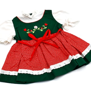 May include: A green and red dress with white lace trim and a red ribbon. The dress has a floral embroidery design on the bodice.