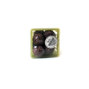 Op de afbeelding: Een groene plastic krat gevuld met donkerbruine chocoladetruffels. Het etiket aan de voorkant luidt "CONFECTIONED BY WILLIAM", "1.25 OZ", "NET WT", "CHOCOLATE TRUFFLES", "ASSORTED", "MADE IN USA".