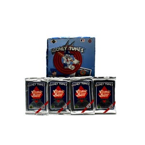 May include: A box of Looney Tunes Comic Ball trading cards featuring Bugs Bunny in a baseball uniform. The box is blue and white with a red circle around Bugs Bunny. There are five packs of cards in front of the box, each with a silver foil design and the words "Looney Tunes Comic Ball" printed on them.