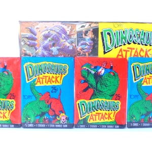 Puede incluir: Un conjunto de cinco paquetes de cartas coleccionables Topps Dinosaurs Attack. Cada paquete contiene 5 cartas, 1 pegatina y 1 chicle. Los paquetes son rojos, azules y amarillos con una ilustración de dinosaurio en la parte delantera. El texto en los paquetes dice "Dinosaurs Attack!" y "25 céntimos".