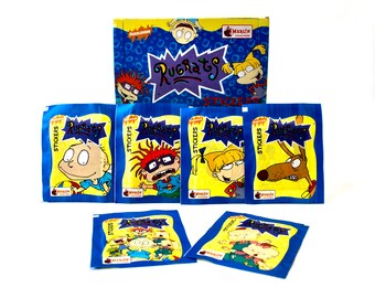 May include: A set of nine Rugrats sticker packs. Each pack features a different Rugrats character, including Tommy Pickles, Chuckie Finster, and Phil and Lil DeVille. The packs are blue with white borders and the words "Rugrats Stickers" printed on them.