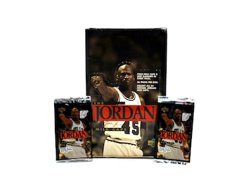 May include: A collection of "The Jordan" milk caps, featuring Michael Jordan. The image shows a box and individual packs with the basketball player's image and the number 45. The box reads "FOUR MILK CAPS & ONE SLAMMER IN EVERY PACK. 36 PACKS PER BOX. COLLECT ALL 54 MICHAEL JORDAN MILK CAPS."