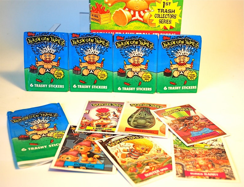 Pu&ograve; includere: Una collezione di figurine e pacchetti di adesivi vintage "Trash Can Trolls". I pacchetti sono blu con un'illustrazione di un troll dei cartoni animati e la scritta "6 Trashy Stickers". Le singole carte presentano vari personaggi e scene di troll.