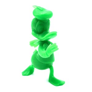 May include: A solid green figurine of Donald Duck in a walking pose. The figure has a hat, a large bill, and outstretched arms. The toy is made of a smooth, solid material and is set against a white background.