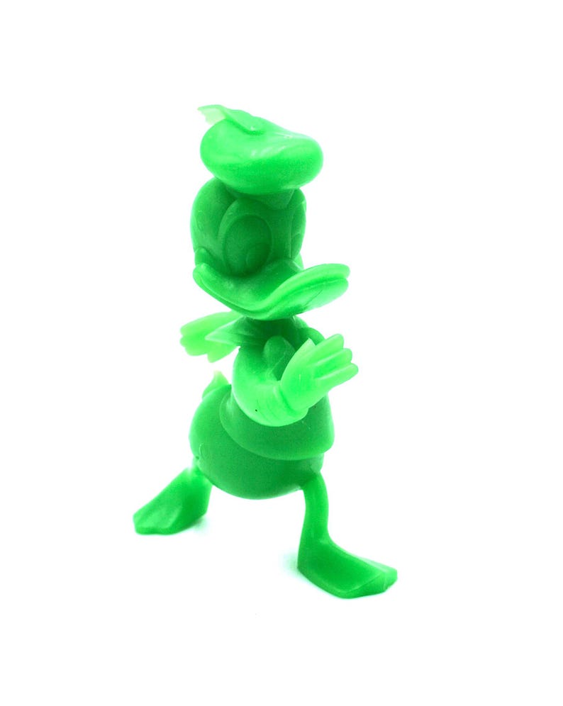 May include: A solid green figurine of Donald Duck in a walking pose. The figure has a hat, a large bill, and outstretched arms. The toy is made of a smooth, solid material and is set against a white background.