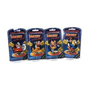 Puede incluir: Cuatro paquetes de cart&oacute;n azul y amarillo con el texto "Classic Collectables" y "MICKEY and his gang!" Cada paquete presenta una imagen de dibujos animados diferente de Mickey Mouse y sus amigos. Los paquetes est&aacute;n etiquetados con "3 TOYS IN 1" y "STAND 'EM UP STICK 'EM UP".