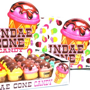 May include: A box of Sundae Cone Candy, a novelty candy shaped like ice cream cones. The box is white with a pink, yellow, and brown ice cream cone design. The candy is arranged in rows in the box. The box is labeled "Sundae Cone Candy" and "T WT 9.6 OZS."
