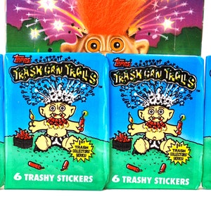 Pu&ograve; includere: Quattro confezioni di adesivi "Trash Can Trolls" di Topps, con un troll dei cartoni animati con i capelli arancioni e un petardo. Le confezioni sono blu e verdi con la scritta "6 Trashy Stickers". Un'immagine pi&ugrave; grande del troll &egrave; visibile sopra.