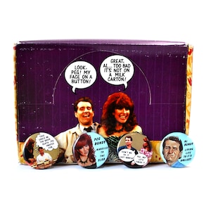 Puede incluir: Un conjunto de ocho botones redondos con personajes del programa de televisión Casados con hijos. Los botones muestran a los personajes Al Bundy, Peg Bundy y Kelly Bundy. Los botones están sobre un fondo morado con una caja blanca.