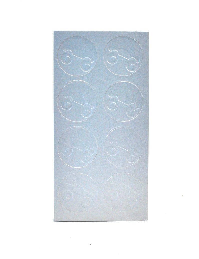May include: A sheet of eight silver-colored stickers. Each sticker is a circle with a raised, embossed design of a small car. The stickers are arranged in two columns of four.