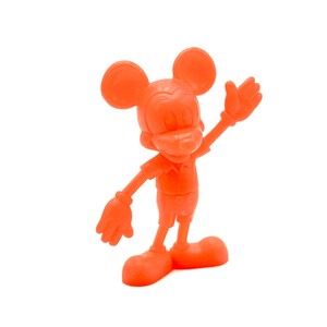 May include: Orange figurine of Mickey Mouse in a classic pose, with one arm raised. The figure has large round ears, a button-up shirt, shorts, and large shoes. The figurine is a solid orange color and stands on a white background.