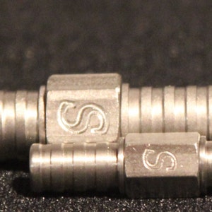 May include: Two silver metal pipe fittings with a ribbed design and the letter "S" engraved on each.