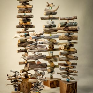 May include: A collection of five vertical sculptures constructed from stacked driftwood pieces and small colorful glass beads. Each sculpture is mounted on a solid wooden block base, featuring varying heights and widths of natural brown wood.