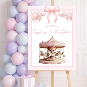May include: A pink and white birthday sign on an easel, featuring a carousel illustration and the text "Welcome to Sophie's 3rd Birthday!" A pink bow and hot air balloons decorate the top. Pastel balloons and wrapped gifts are in the background.