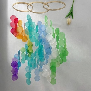 May include: A vibrant, rainbow-coloured mobile composed of numerous iridescent, circular discs. The discs are suspended from three wooden hoops, creating a decorative, eye-catching piece. The colour gradient transitions from red to purple, green, and blue.