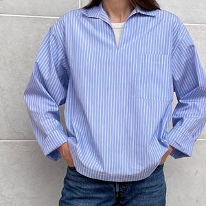 Op de afbeelding: Een lichtblauw en wit gestreept overhemd met kraag en een enkele borstzak. Het overhemd heeft lange mouwen en wordt gecombineerd met een blauwe jeans.