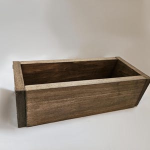 May include: A rectangular wooden box with a dark brown stain. The box has a simple, open design with visible wood grain. The box is suitable for storage or display.