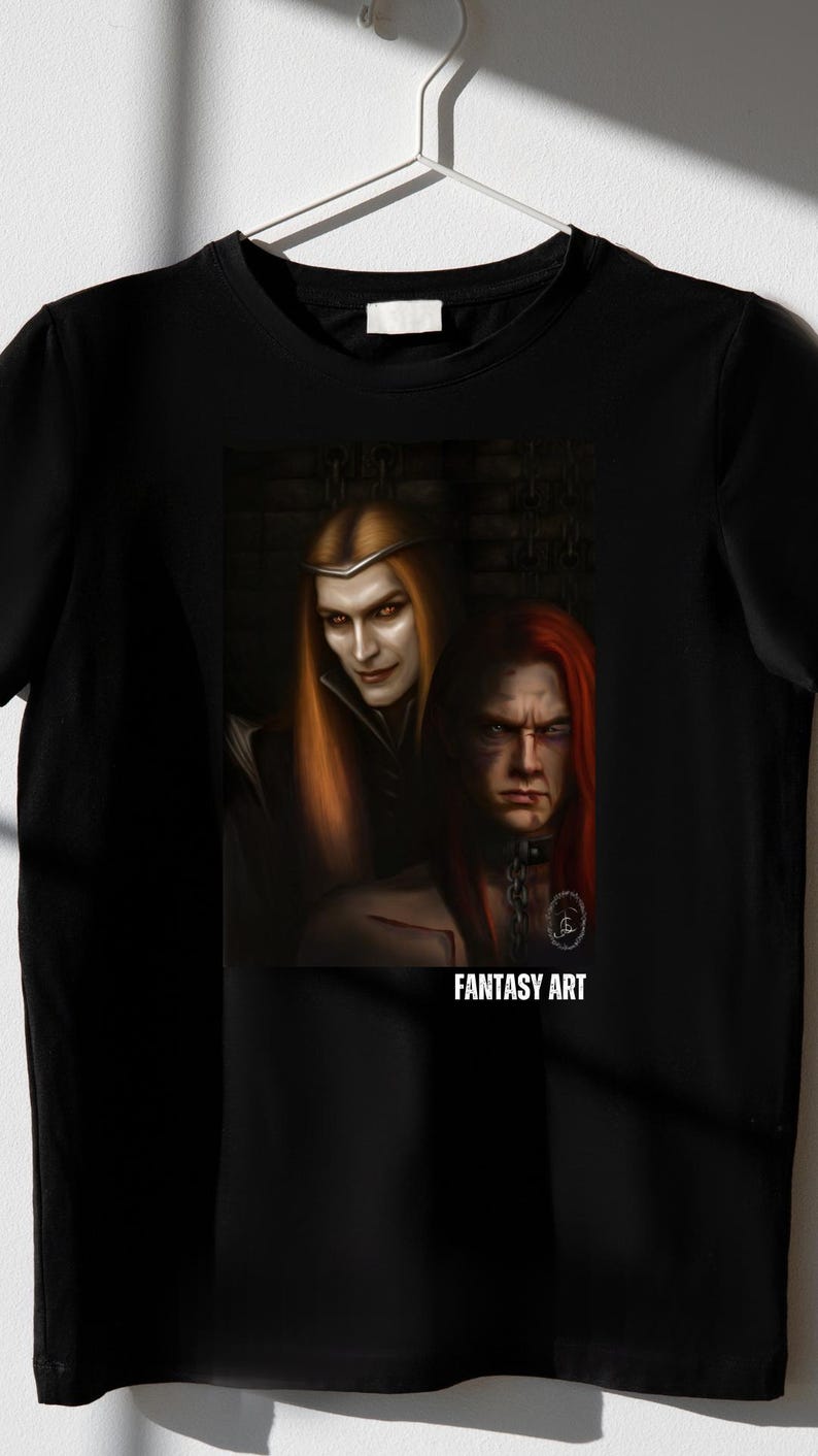 Op de afbeelding: Zwart t-shirt met een fantasy art print. De afbeelding toont twee figuren met lang haar, &eacute;&eacute;n blond en &eacute;&eacute;n roodharig, in een donkere, gotische stijl. De tekst "FANTASY ART" staat eronder.
