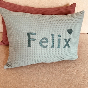 A handcrafted old green waffle weave cotton cushion with custom name embroidery, featuring a hidden zip closure and a soft hypoallergenic insert for nursery decor.

Ein handgemachtes Waffelkissen in Altgrün mit personalisierter Namensstickerei, nahtverdecktem Reißverschluss und antiallergischem Innenkissen für das Babyzimmer.

Un coussin gaufré artisanal en vert vieilli avec broderie personnalisée du prénom, fermeture éclair invisible et coussin intérieur hypoallergénique.