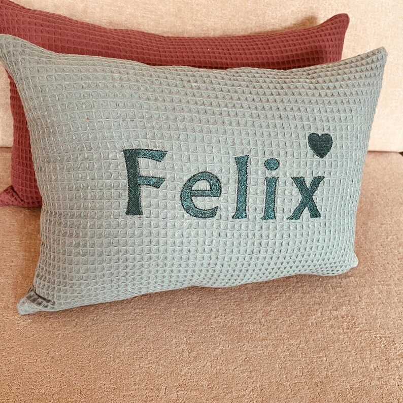 A handcrafted old green waffle weave cotton cushion with custom name embroidery, featuring a hidden zip closure and a soft hypoallergenic insert for nursery decor.

Ein handgemachtes Waffelkissen in Altgrün mit personalisierter Namensstickerei, nahtverdecktem Reißverschluss und antiallergischem Innenkissen für das Babyzimmer.

Un coussin gaufré artisanal en vert vieilli avec broderie personnalisée du prénom, fermeture éclair invisible et coussin intérieur hypoallergénique.
