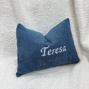 May include: A rectangular blue pillow with a textured, plush surface. The name Teresa is embroidered in white cursive script across the center of the pillow. The pillow has a soft, fuzzy appearance and is positioned against a white textured background.
