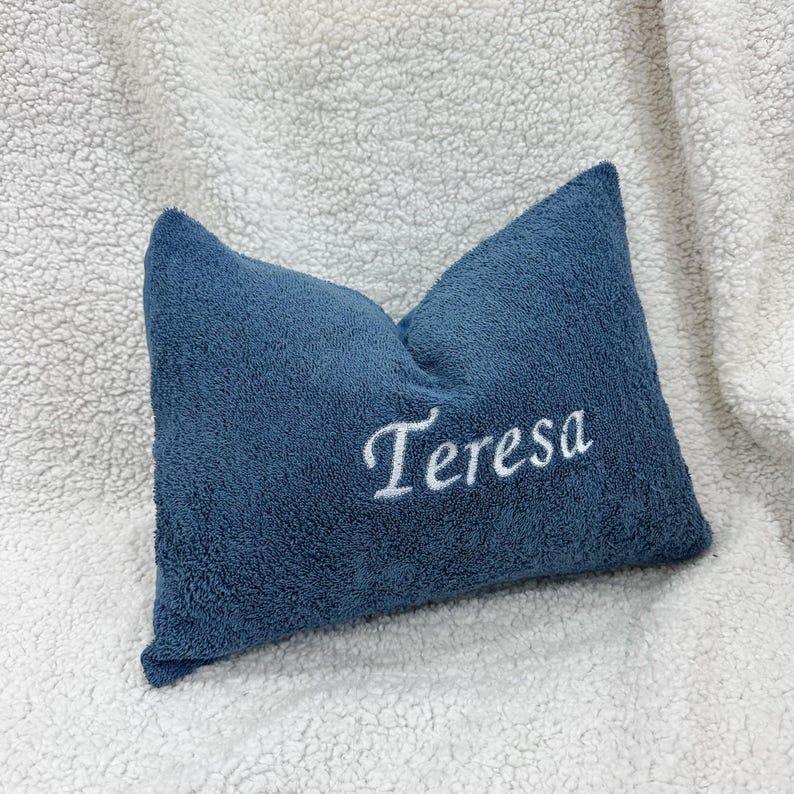 May include: A rectangular blue pillow with a textured, plush surface. The name Teresa is embroidered in white cursive script across the center of the pillow. The pillow has a soft, fuzzy appearance and is positioned against a white textured background.