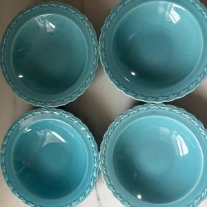 May include: Four turquoise-colored ceramic bowls. Each bowl has a round shape with a slightly raised center and a decorative, textured border. The bowls are arranged in a square pattern, offering a cohesive set.