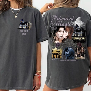 以下が含まれることがあります： チャコールグレーのTシャツ。胸元には家と「Practical Magic」の文字が小さくプリントされています。背面には映画のシーンのコラージュ、満月、そして装飾的なフォントで「Practical Magic」の文字が大きくデザインされています。