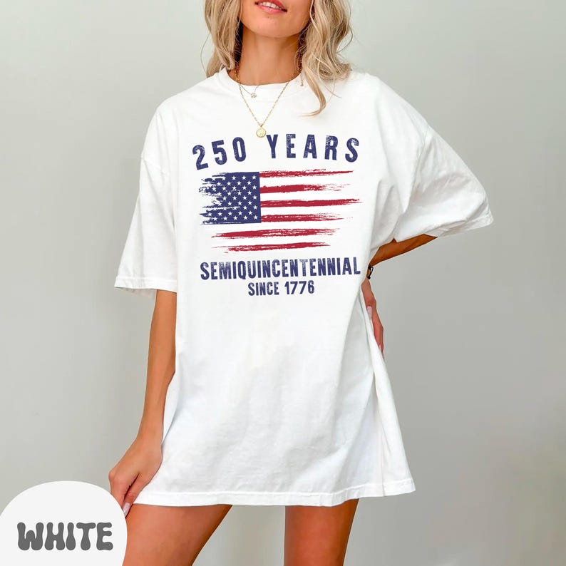 May include: White t-shirt featuring a distressed American flag design with the text "250 YEARS SEMIQUINCENTENNIAL SINCE 1776" in navy blue. The shirt has short sleeves and a relaxed fit.