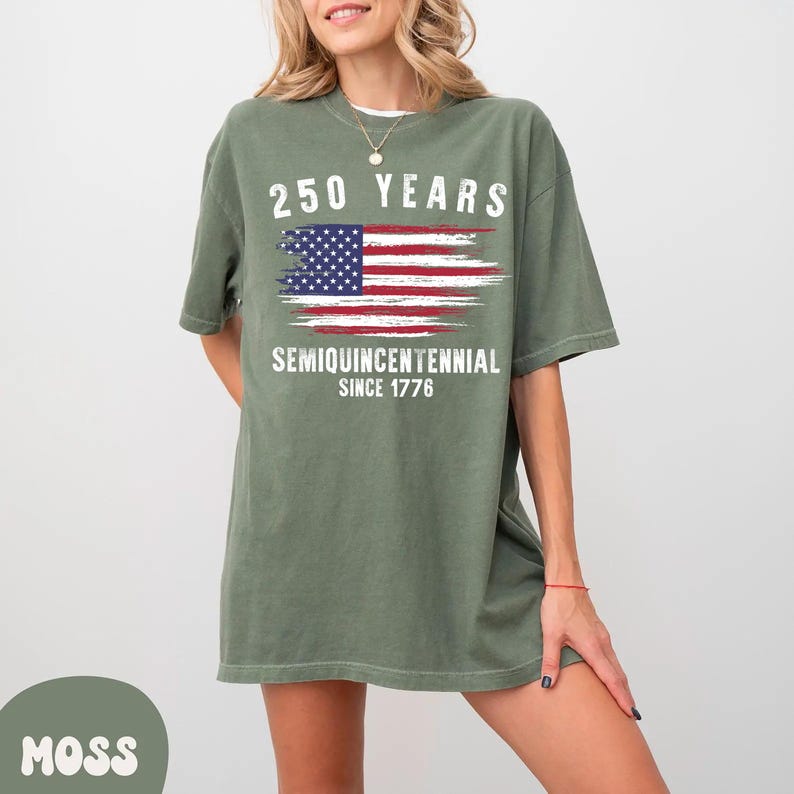 May include: Moss green t-shirt with the text "250 YEARS" above a distressed American flag graphic. Below the flag are the words "SEMIQUINCENTENNIAL SINCE 1776". The shirt is a relaxed fit.