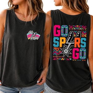 Puede incluir: Una camiseta sin mangas negra con un peque&ntilde;o gr&aacute;fico en el pecho que incluye el texto "GO GO" y un logotipo de equipo. La parte trasera muestra un gr&aacute;fico grande y colorido con el texto "GO SPURS GO" rodeado de patrones geom&eacute;tricos ne&oacute;n.