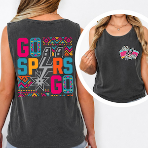 Puede incluir: Una camiseta sin mangas de color gris carb&oacute;n con un gr&aacute;fico grande en la espalda con el texto GO SPURS GO en rosa brillante, naranja y azul, acentuado por patrones geom&eacute;tricos y un logo de espuela plateado. Un logo m&aacute;s peque&ntilde;o est&aacute; en el pecho.