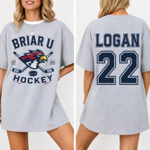 May include: A heather gray short-sleeve t-shirt featuring a Briar U Hockey graphic with a bird mascot and crossed hockey sticks on the front. The back displays the name LOGAN and the number 22 in large dark blue block lettering.