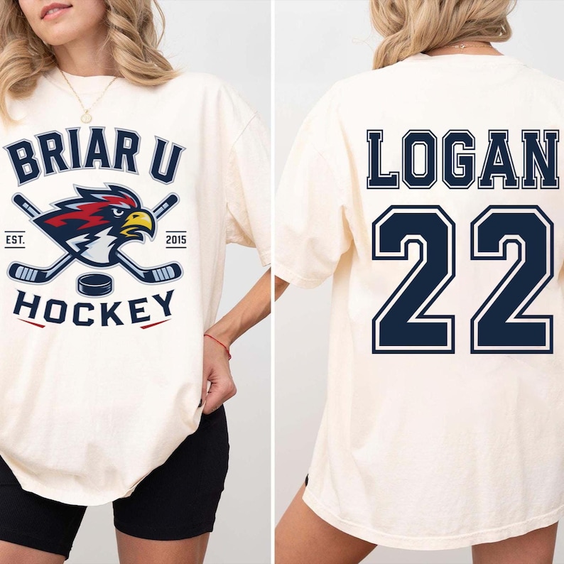 May include: An off-white short-sleeve t-shirt featuring a Briar U Hockey graphic on the front with a cardinal bird mascot, hockey sticks, and a puck. The back of the shirt displays the name Logan and the number 22 in large dark blue block lettering.