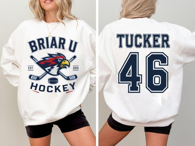 May include: A white crewneck sweatshirt featuring a front graphic of a red and blue bird mascot with two crossed hockey sticks and a puck, with the text BRIAR U HOCKEY EST 2015. The back displays the name TUCKER and the number 46 in navy blue.