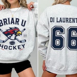 May include: A light gray crewneck sweatshirt featuring a Briar U Hockey graphic on the front with a bird mascot and hockey sticks, and the name DI LAURENTIS with the number 66 printed in large dark blue block letters on the back.