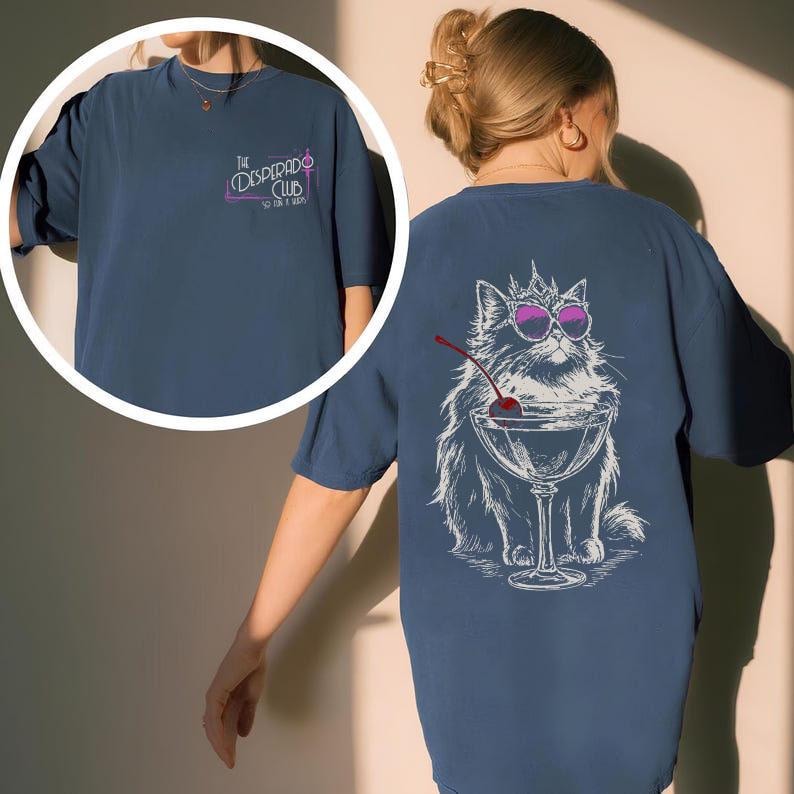 May include: Navy blue t-shirt with a graphic of a cat wearing sunglasses and a crown, sitting in a martini glass with a cherry. The front of the shirt has the text "The Desperado Club".