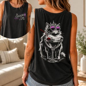 May include: Black tank top featuring a graphic of a cat wearing sunglasses and a crown, sitting in a martini glass with a cherry. The front of the tank top has the text "The Desperado Club".